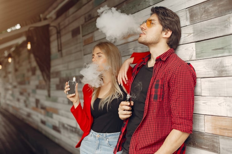 Two people vaping against a wooden wall